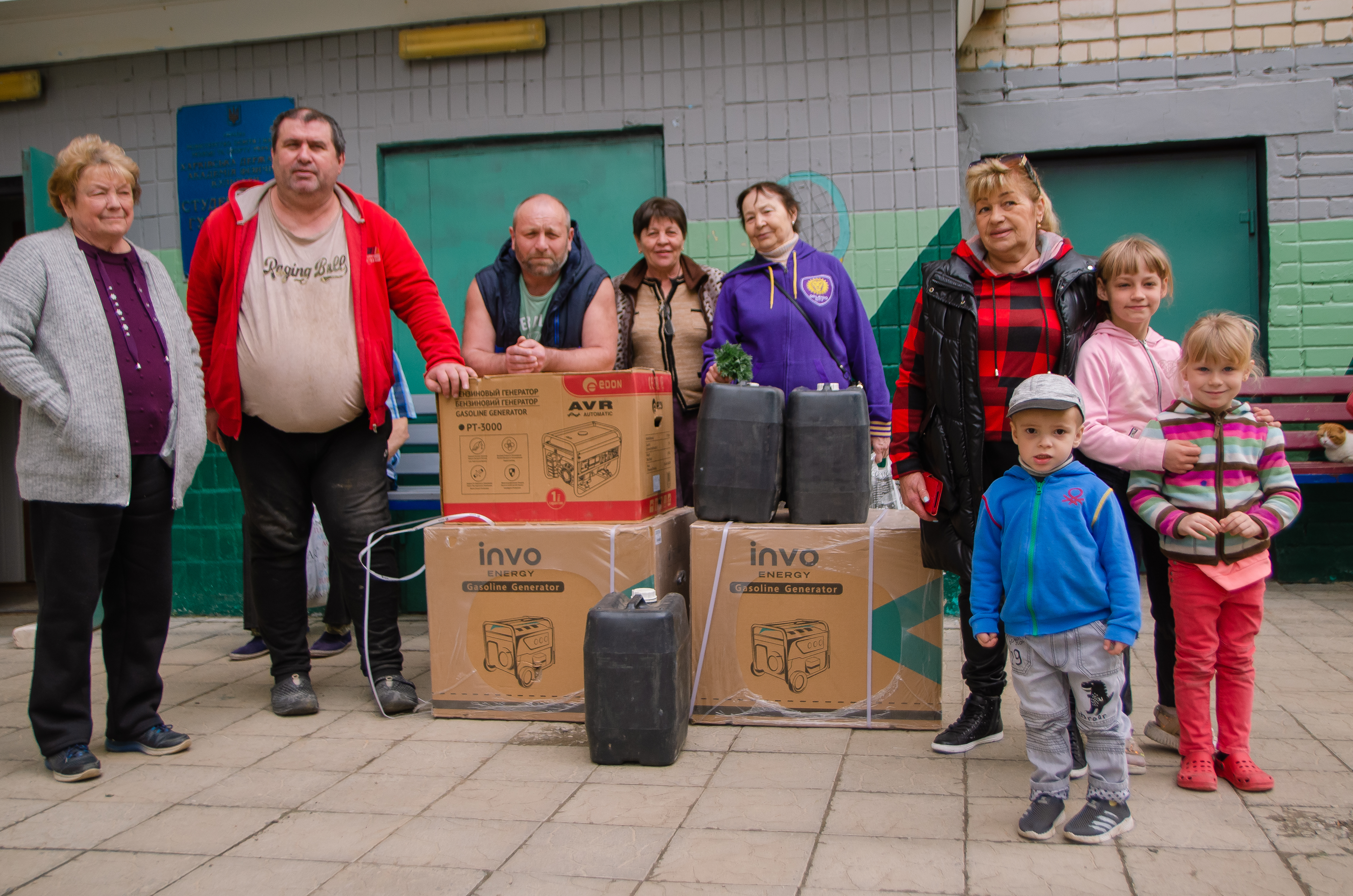 Группа из шести человек - шестеро взрослых и троих детей в зимней одежде стоят на улице рядом с несколькими новыми генераторами электричества